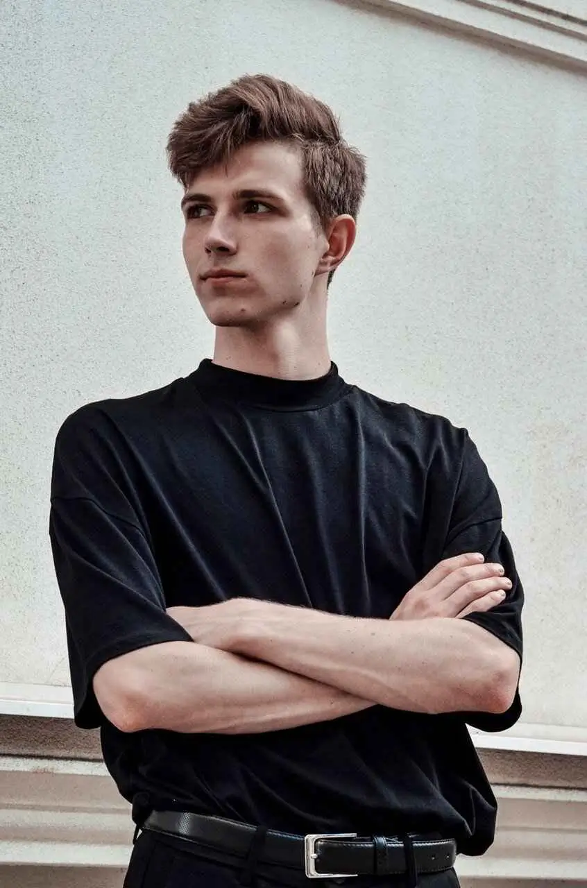 Portrait picture of boy standing with his hands crossing, wearing black t-shirt on white background